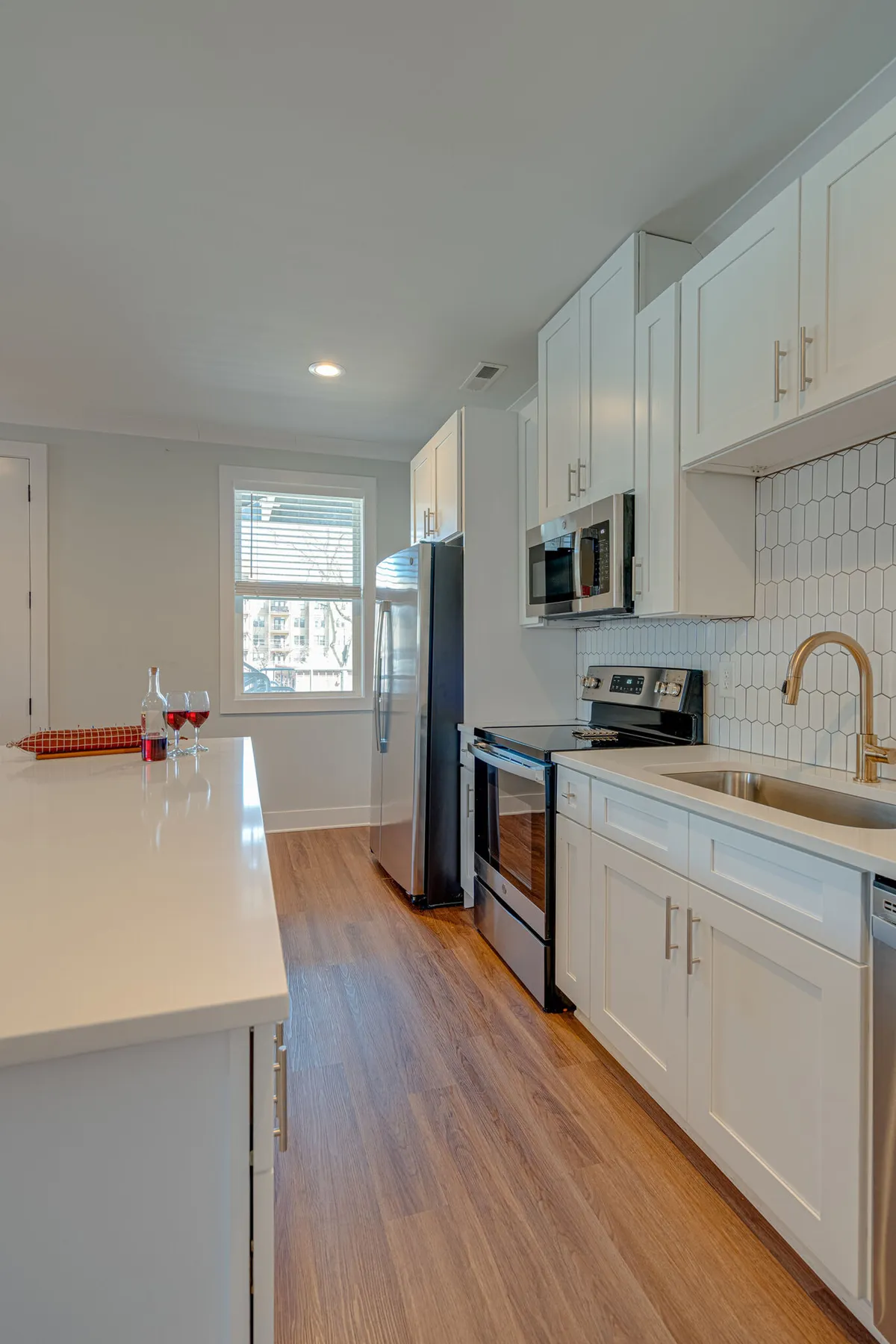 A light-filled, modern kitchen with white cabinetry, a hexagonal backsplash, stainless steel appliances, and an inviting island with ample countertop space. The setting is perfect for cooking, baking, and gathering friends or family.
