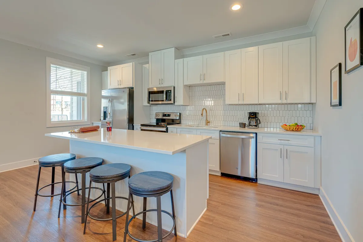 A contemporary kitchen with a large island featuring seating, gleaming stainless steel appliances, white cabinetry, and a striking tile backsplash. The layout is spacious and encourages both cooking and socializing, making it ideal for gatherings and celebrations.