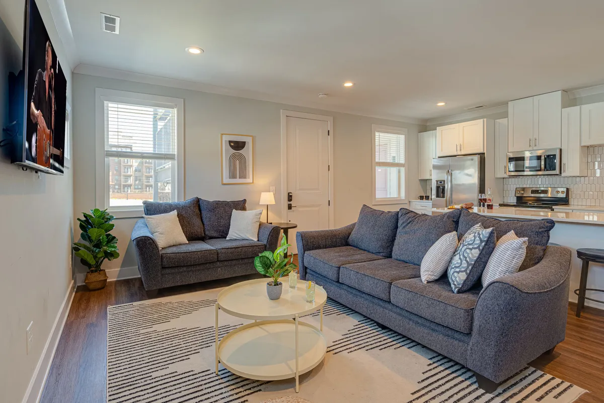 The image showcases a beautifully arranged living room with plush sofas, a stylish coffee table, lush plants, and vibrant wall art. The inviting space exudes comfort and warmth, encouraging guests to relax, socialize, or celebrate together.