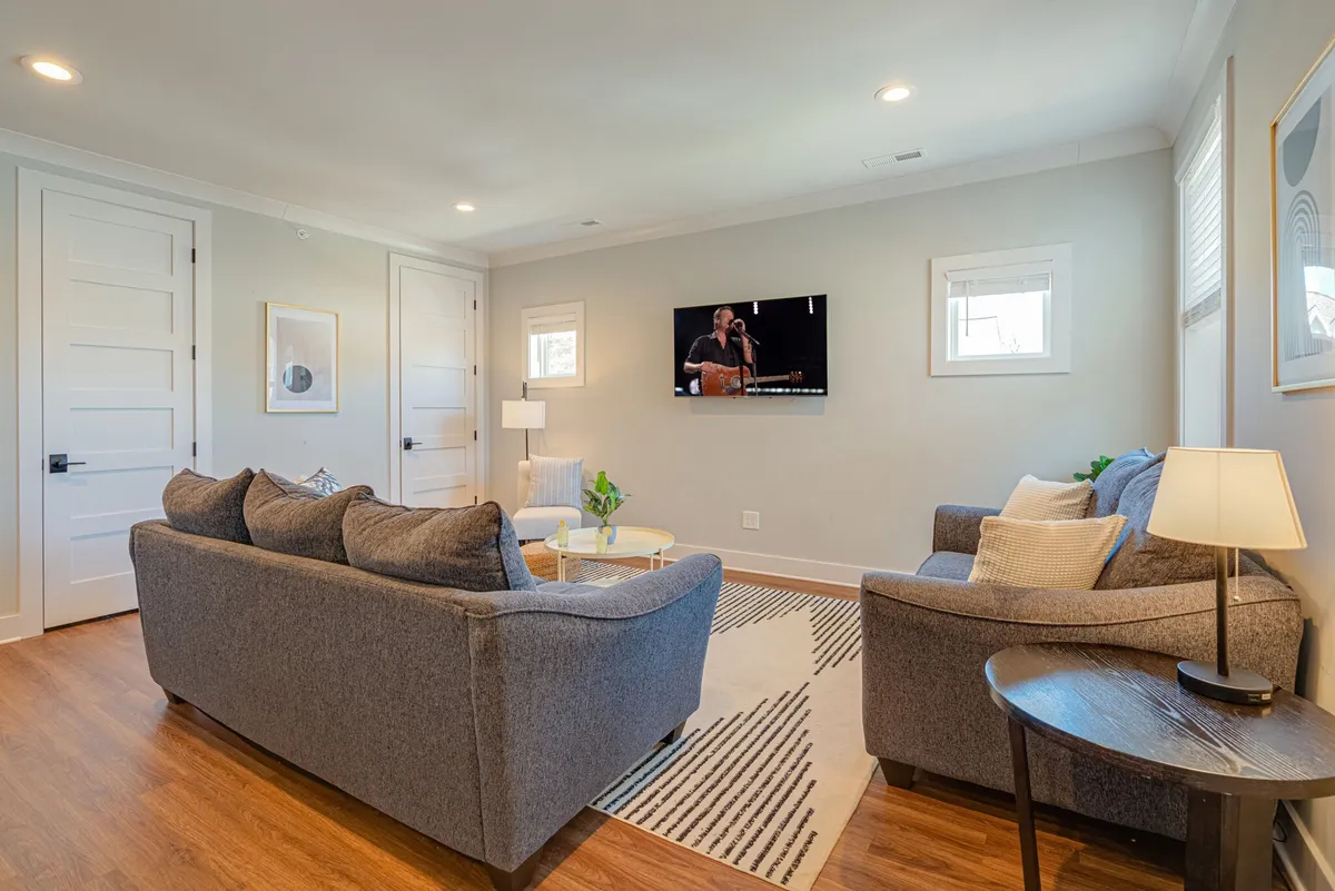 A modern, cozy living area featuring multiple sofas arranged for conversation, a large television, a coffee table, and a decorative plant that adds a touch of freshness. The room has a clean and contemporary look, ideal for both relaxation and group activities.
