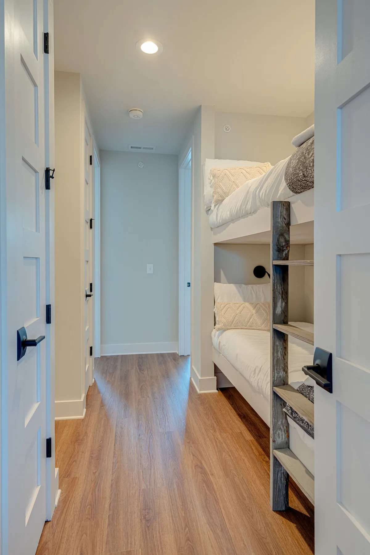 A cozy built-in hallway bunk bed setup with wooden ladders and doorways leading to other rooms. The beds are neatly made, suggesting a playful and functional sleeping area ideal for kids or extra guests.