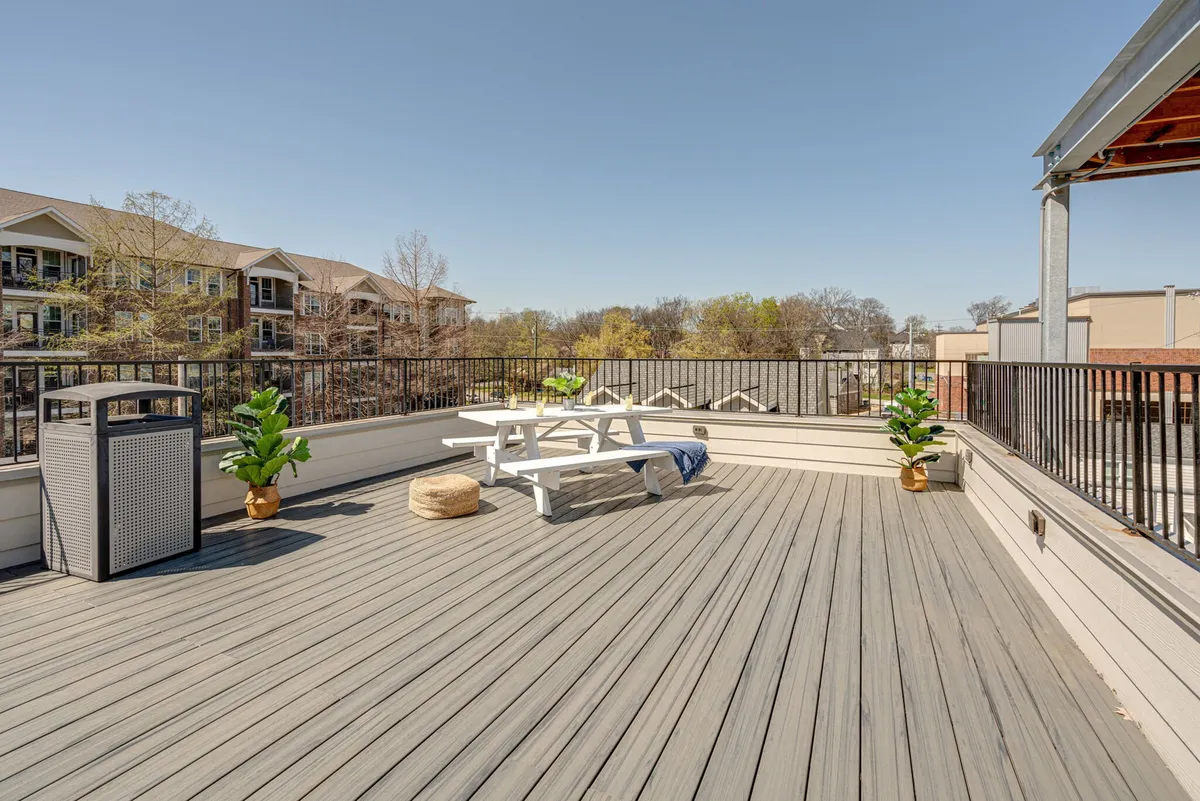 An exterior patio with a picnic table, potted plants, and a casual outdoor dining vibe. The scene is welcoming and relaxed, ideal for families or groups to gather and enjoy meals or downtime in a sunny, accessible setting.